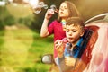 The more bubbles, the better. two happy children blowing bubbles while leaning out of a car window together.