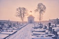 Morgue on a misty cemetery with a shining bell-cot with sunflare. Royalty Free Stock Photo
