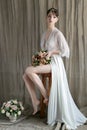 Morning beautiful delicate bride with short hair with a small wreath silk underwear sitting on a chair with a wedding bouquet Royalty Free Stock Photo