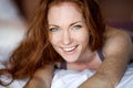 Morning in bed, a young charming red-haired woman with freckles lying in bed, hugging pillow, smiling, enjoying the Royalty Free Stock Photo