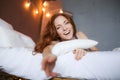 Morning in bed, a young charming red-haired woman with freckles lying in bed, hugging pillow, smiling, enjoying the Royalty Free Stock Photo