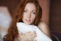 Morning in bed, a young charming red-haired woman with freckles lying in bed, hugging pillow, smiling, enjoying the Royalty Free Stock Photo