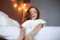 Morning in bed, a young charming red-haired woman with freckles lying in bed, hugging pillow, smiling, enjoying the Royalty Free Stock Photo