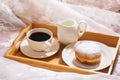 Morning breakfast in bed with fresh coffee, milk and doughnut in powdered sugar, in white dishes on a wooden tray. Royalty Free Stock Photo