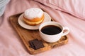 Morning breakfast in bed with fresh and delicious coffee, a doughnut in powdered sugar and three slices of chocolate on a wooden Royalty Free Stock Photo