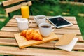 Morning Breakfast In Green Garden With French Croissant, Coffee Cup, Orange Juice, Tablet and Notes Book On Wood Table Royalty Free Stock Photo