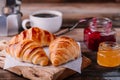 Homemade baked croissants with jam and coffee on wooden rustic background