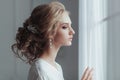 Morning of the bride. Beautiful young woman in elegant white robe with fashion wedding hairstyle standing near the Royalty Free Stock Photo