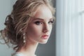Morning of the bride. Beautiful young woman in elegant white robe with fashion wedding hairstyle standing near the