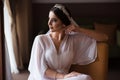 Morning bride in a hotel room. Bride brunette with makeup and a tiara in her hair sits in a chair and looks out the window