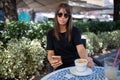 Morning in cafe - attractive woman in black dress and dark sunglasses drinkin coffe and make selfie photo for social networks Royalty Free Stock Photo