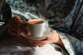 Morning coffee in bed. A cup of coffee in female hands in the morning sun. Enjoying the little things. Closeup