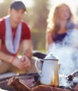 Morning coffee on the brew. Coffee brewing on an outdoor camp fire with a young couple in the background.