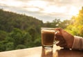 Morning coffee concept. hand holding hot coffee cup with lush green jungle background, sunrise through the forest, copy-space Royalty Free Stock Photo