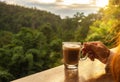 Morning coffee concept. hand holding hot coffee cup with lush green jungle background, sunrise through the forest, copy-space Royalty Free Stock Photo