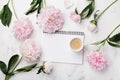 Morning coffee cup for breakfast, empty notebook and pink peony flowers on white stone table top view in flat lay style.