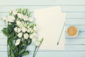 Morning coffee cup, empty paper list, pencil, and bouquet of white flowers eustoma on blue rustic table from above. Woman desk.