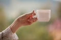 Morning coffee cup. Female hand holds white cup of morning hot drink - coffee or tea on the balcony on the background of mountain Royalty Free Stock Photo