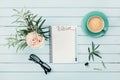 Morning coffee cup, notebook with to do list, pencil, eyeglasses and vintage rose flower in vase on blue rustic table from above.