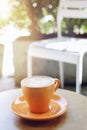 Morning coffee hot latte in orange cup with saucer on wood table coffee shop garden blurred background Royalty Free Stock Photo