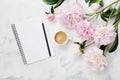 Morning coffee mug for breakfast, empty notebook, pencil and pink peony flowers on white stone table top view in flat lay style. Royalty Free Stock Photo