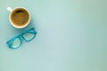 A morning coffee mug and a pair of blue reading glasses