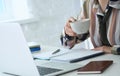 Morning coffee before a productive working day. Young female office worker holding coffee cup and looking at the laptop