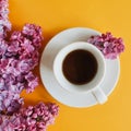 Morning coffee in a white cup with fragrant lilac flowers on a yellow cheerful background. Aroma concept, good morning.