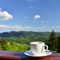 Morning cup of coffee with a beautiful mountain landscape background. White cup and saucer - espresso on a wooden table. Royalty Free Stock Photo