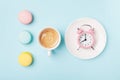 Morning cup of coffee, cake macaron and alarm clock on light turquoise table top view. Flat lay style. Beautiful breakfast.