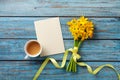Morning cup of coffee, clean card and spring daffodil flowers on blue wooden table. Beautiful breakfast for Women day, Mother day. Royalty Free Stock Photo