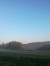 Morning fog on meadow with trees and hills with forest silhouettes Royalty Free Stock Photo