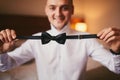 Morning of the groom before the wedding. Groom morning preparation. Young and handsome groom getting dressed in a wedding bow tie