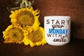 Morning inspirational words on white mug of coffee - Start your Monday with a smile. With sunflowers blossom arrangement.