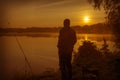 Morning on the lake dawn. A fisherman is standing on the shore next to fishing rods