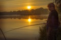 Morning on the lake dawn. A fisherman is standing on the shore next to fishing rods