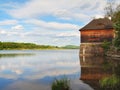 Morning lake with old style wooden fishing hut on the right bank, reflection of sky Royalty Free Stock Photo