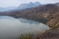 Morning landscape with silhouette in sunlight of strong mountains on horizon in haze and quiet calm water of river with reflection Royalty Free Stock Photo