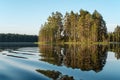 Morning landscape, smooth, calm lake, island with pine and reflection of trees in the water, blue sky and forest shore at dawn. Royalty Free Stock Photo