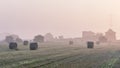 The morning mist of dawn covers the fields of the Tuscan countryside where hay bales lie, Italy Royalty Free Stock Photo