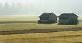 Morning mist in a mountain valley with fields and old wooden barns and forest behind Royalty Free Stock Photo