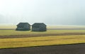 Morning mist in a mountain valley with fields and old wooden barns and forest behind Royalty Free Stock Photo