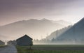 Morning mist in a mountain valley with fields and old wooden barns and lattice cross power lines and mountains in silhouette behin