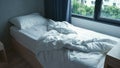 Morning at modern bedroom - crumpled bed with white bed linens, sheet, pillows, blanket, curtains and window Royalty Free Stock Photo