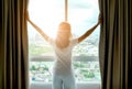 Morning of a new day woman wake up in the bedroom with her refreshing. She stand at the window , raised her two arms and look city
