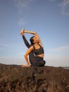 Morning outdoor yoga practice near the ocean. Asian woman practicing Eka Pada Sirsasana, Foot-behind-the-Head Pose. Flexible Royalty Free Stock Photo