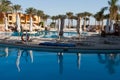 Morning pool side in hotel. No people near swimming pool. Closed pool umbrellas. Water pool reflex in the calm water. Palms on sea