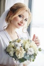 Morning portrait of the bride preparing for the wedding ceremony. Portrait of a blonde woman near the window in a white robe Royalty Free Stock Photo