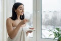 Morning portrait of young beautiful woman in bath towel with cup of fresh coffee near the window Royalty Free Stock Photo