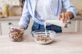 Morning routine concept. Young woman pouring fresh milk from glass into bowl with cereals, having breakfast Royalty Free Stock Photo